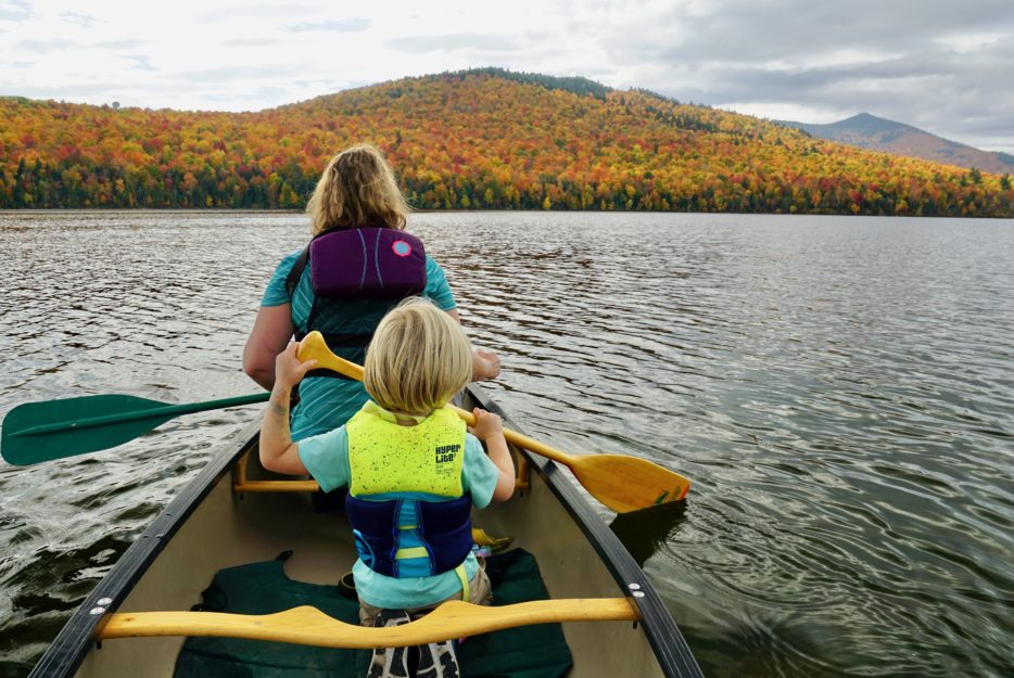 Mom and kid paddle canoe with lifejackets on. 