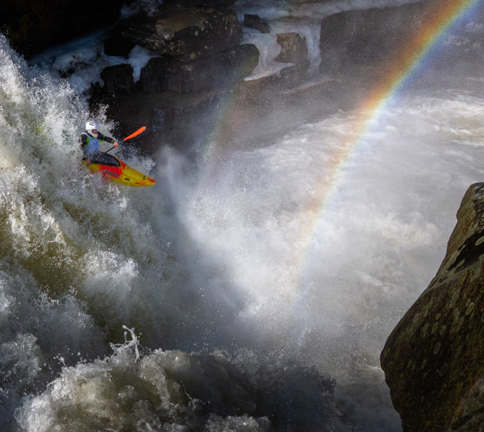 Kayaker with rainbow over waterfall.