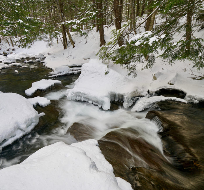 Water flows down a cascade surrounded by snow and ice. 