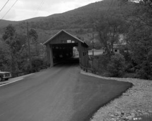 Black and White photo of a covered bridge from the road. 