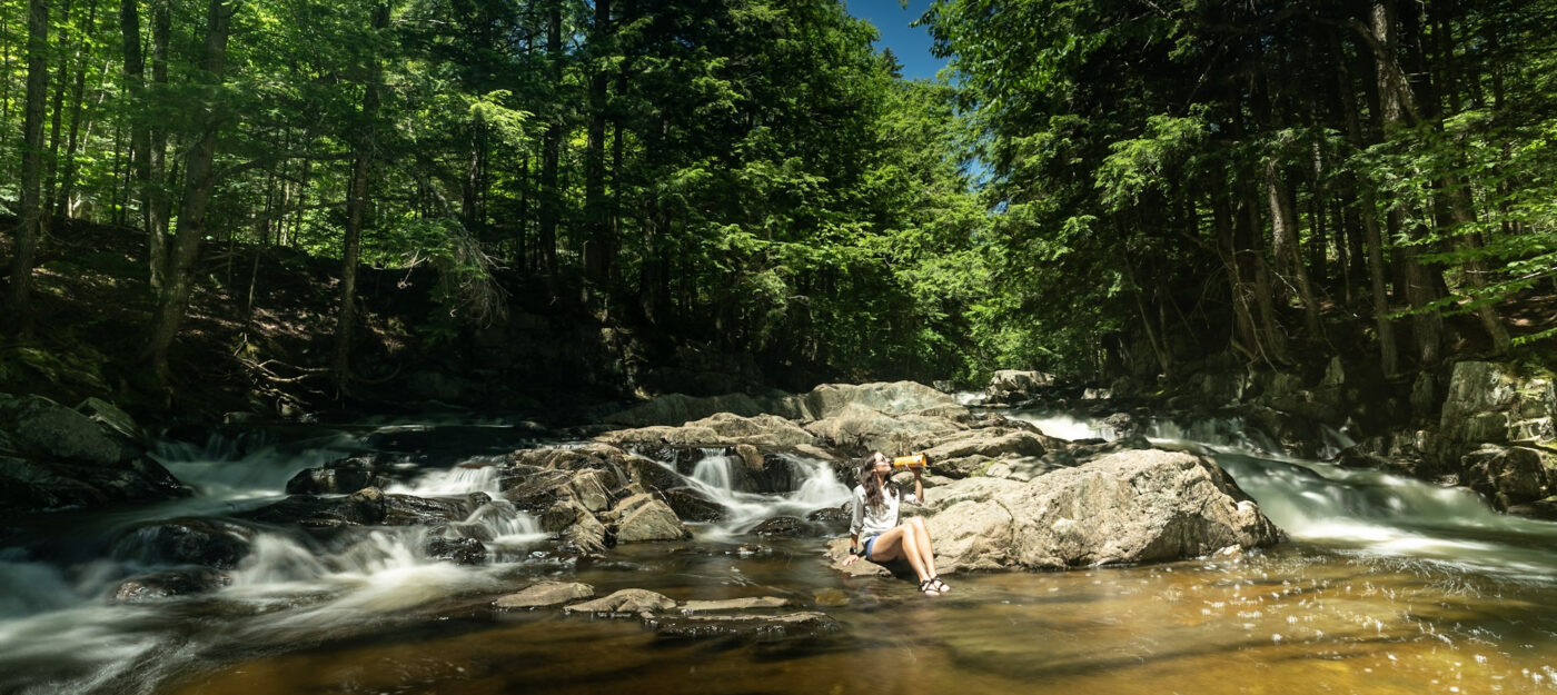 Woman sits on a rock drinking water